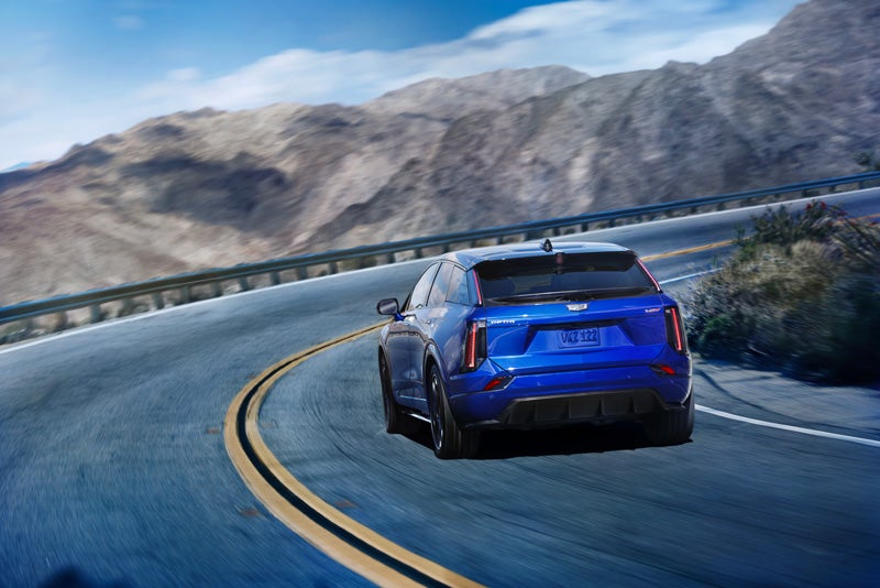 Rear View of a Blue 2026 OPTIQ-V Driving on a Curve of a Mountain Row | Earnhardt Chandler Cadillac in Chandler AZ